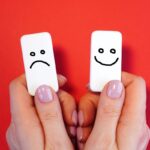 Due pedina domino in mano: una con disegnata la faccina triste e l'altra felice