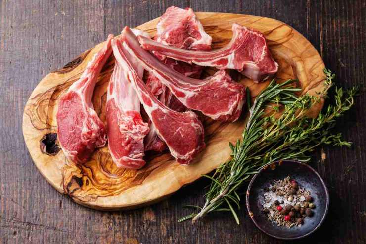 Agnello crudo sopra ad un tagliere con a fianco gli ingredienti per la preparazione