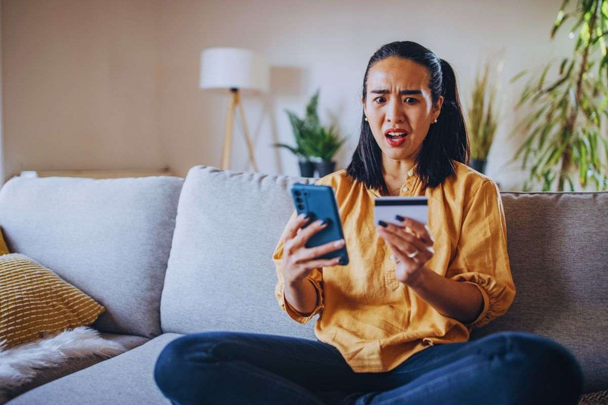 Donna con espressione sconvolta tiene telefono e carta di credito in mano