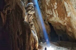 Fascio di luce entra da una grotta, persone sul fondo