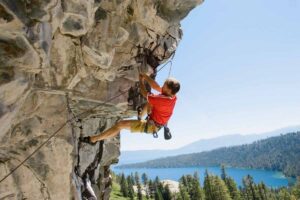 Uomo fa arrampicata su roccia con sfondo mare e vegetazione