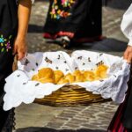 Donne vestite in modo tradizionale di nero con fiori tengono cesto con panini