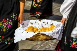 Donne vestite in modo tradizionale di nero con fiori tengono cesto con panini