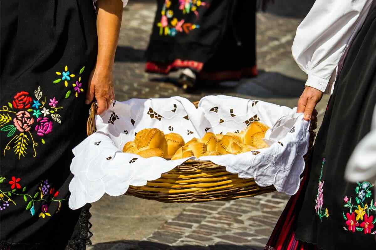 Donne vestite in modo tradizionale di nero con fiori tengono cesto con panini