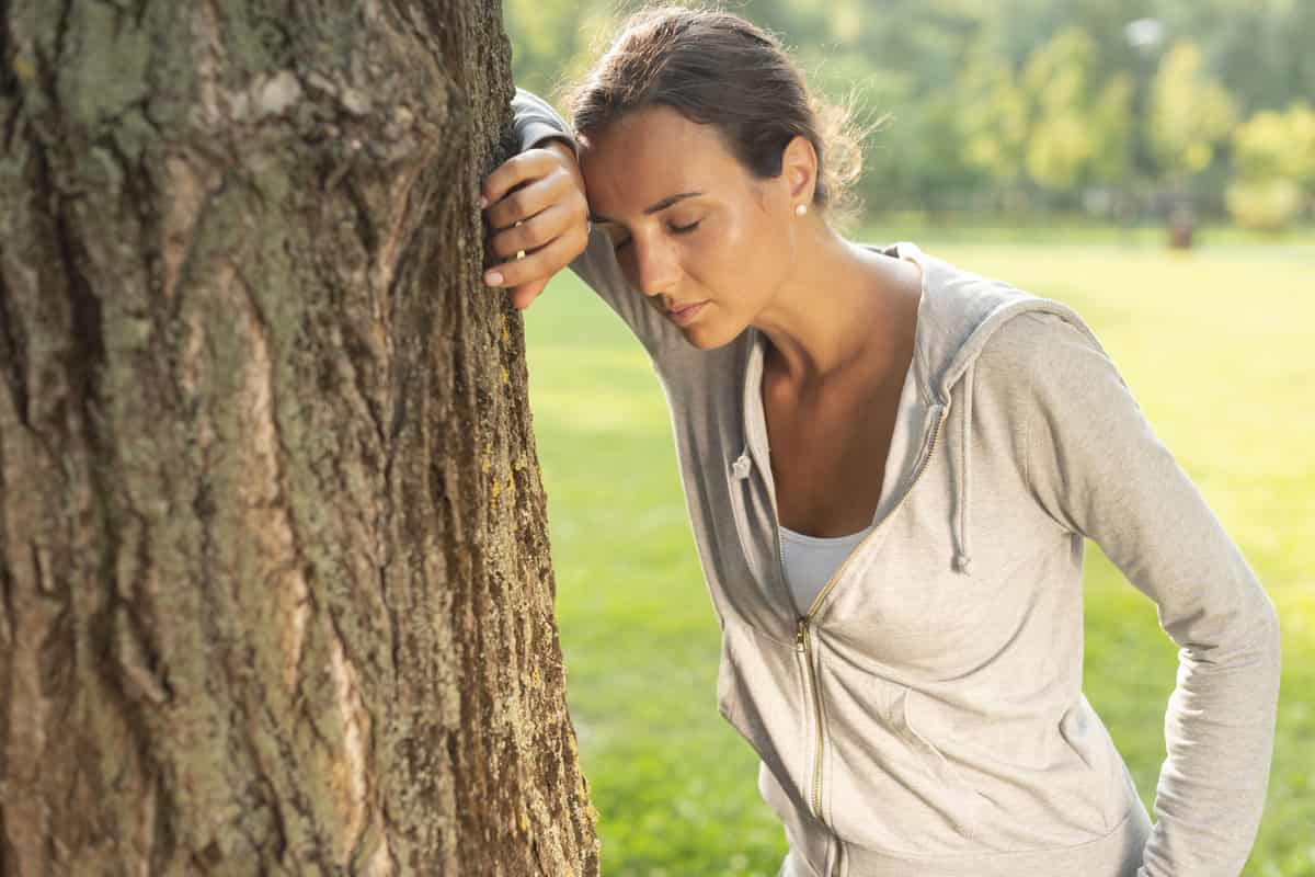 Donna stanca appoggiata a un albero