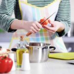 Mani di donna con grembiule in cucina che tagliano pomodoro