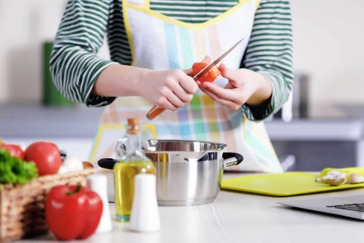 Mani di donna con grembiule in cucina che tagliano pomodoro