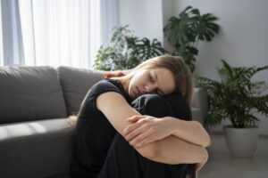 Ragazza che si abbraccia le ginocchia vicino a una finestra da cui entra luce
