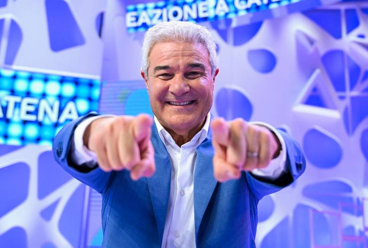 Pino Insegno indica felice la telecamera