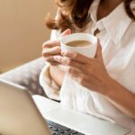 Donna con tazza di caffè in mano e PC davanti a lei