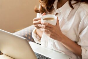 Donna con tazza di caffè in mano e PC davanti a lei