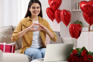 Donna davanti al pc con regalo, palloncini a forma di cuore e rose rosse