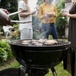 Uomo che prepara un barbecue accanto a un gruppo di persone