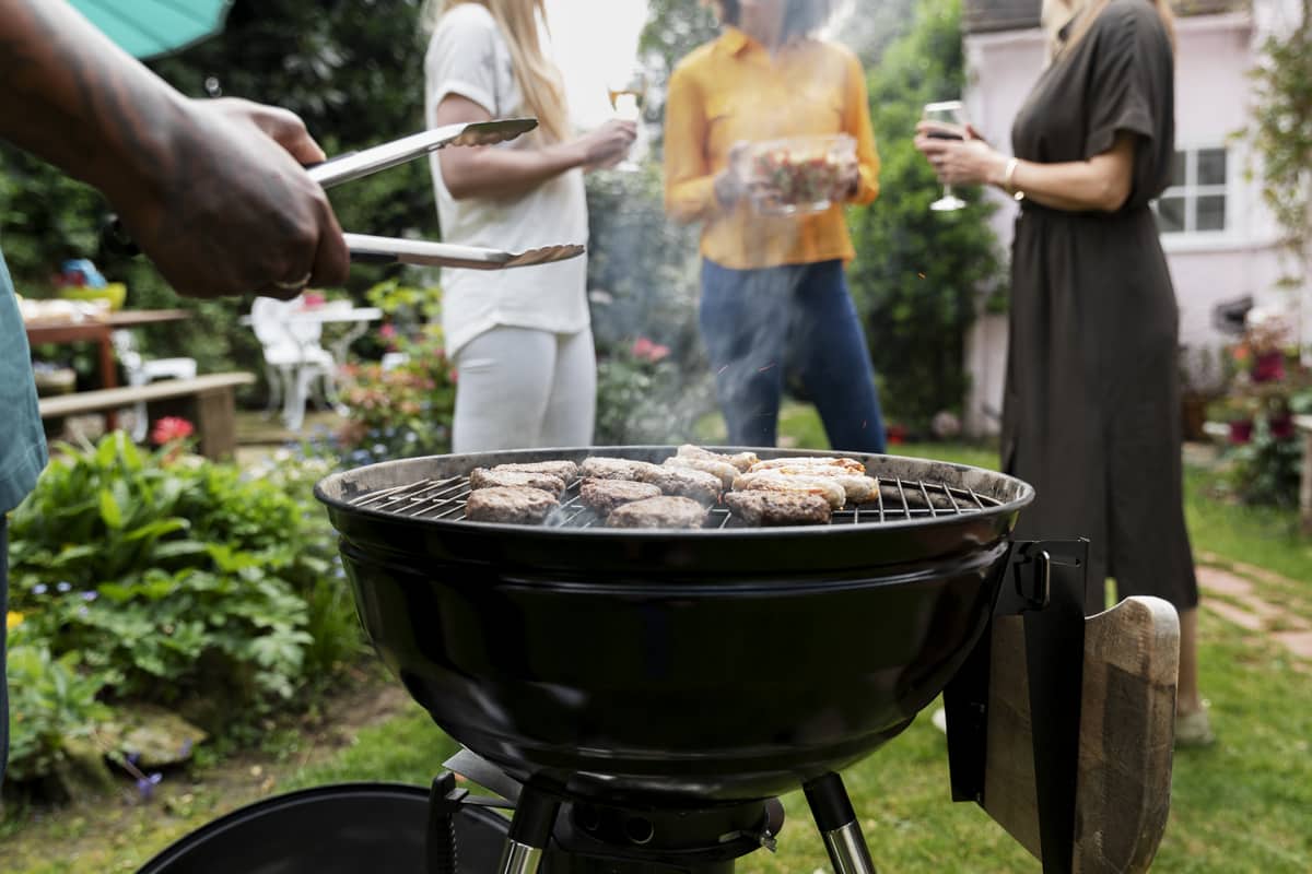 Uomo che prepara un barbecue accanto a un gruppo di persone