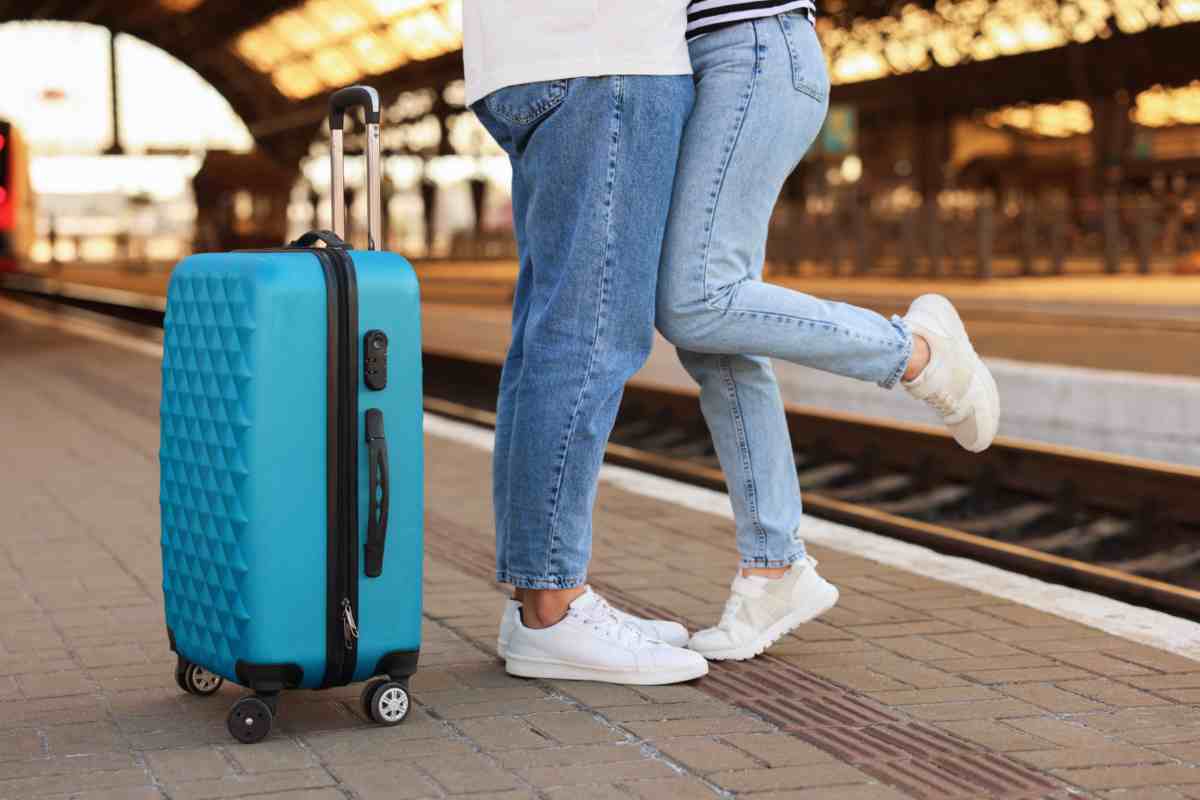 Due persone con valigia che si abbracciano alla stazione