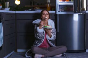 Donna che mangia in cucina di notte seduta a terra