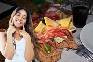 Ragazza con dita sulle guance, sorridente, dietro di lei tagliere salumi e formaggi e vino