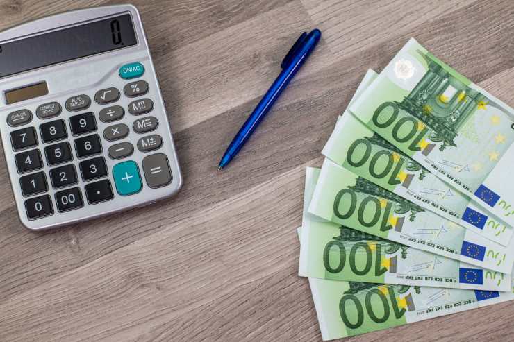 Calcolatrice, penna e banconote da 100€ sopra a un tavolo di legno