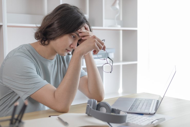 donna triste con occhiali in mano e cuffie e pc sul tavolo