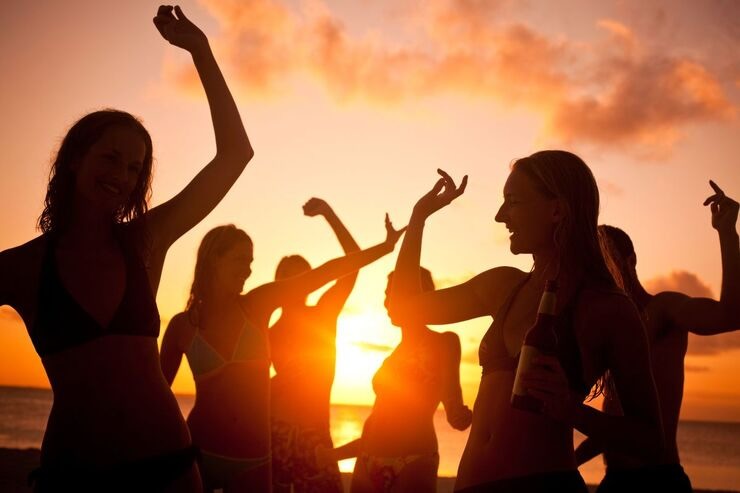 Giovani ragazzi e ragazze ballano in spiaggia al tramonto