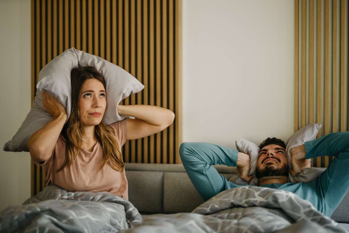 coppia a letto con cuscini nelle orecchie per il troppo rumore