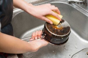 Donna che lava una pentola incrostata con spugna